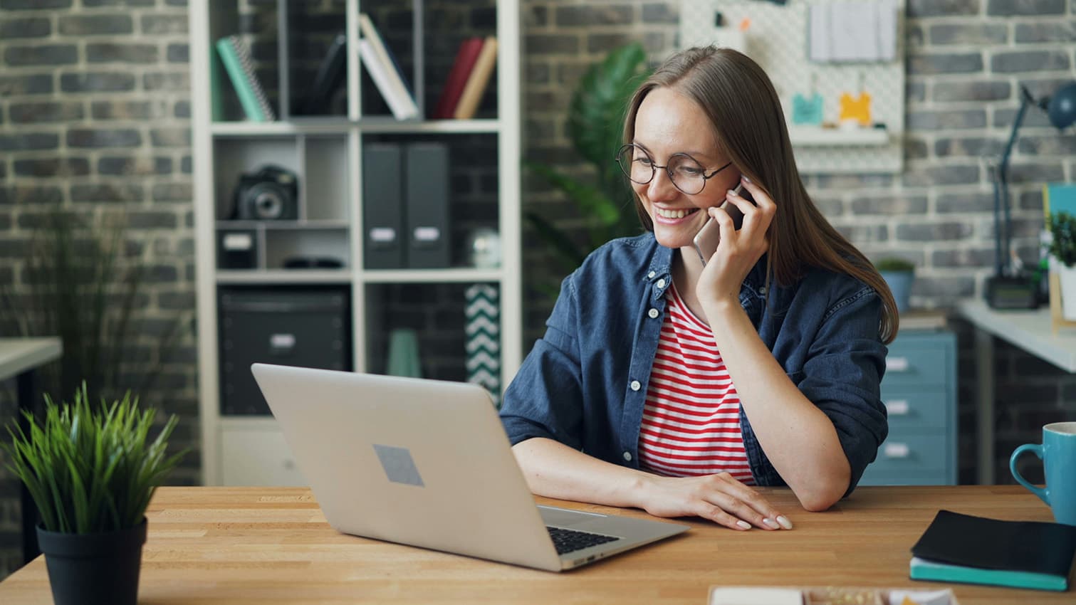 Professional woman having a phone conversation while using a laptop in an office space