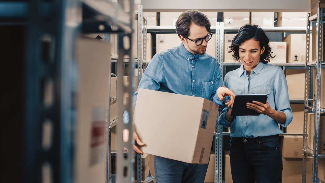 Two employees managing stock levels, with one holding a package and the other using a tablet